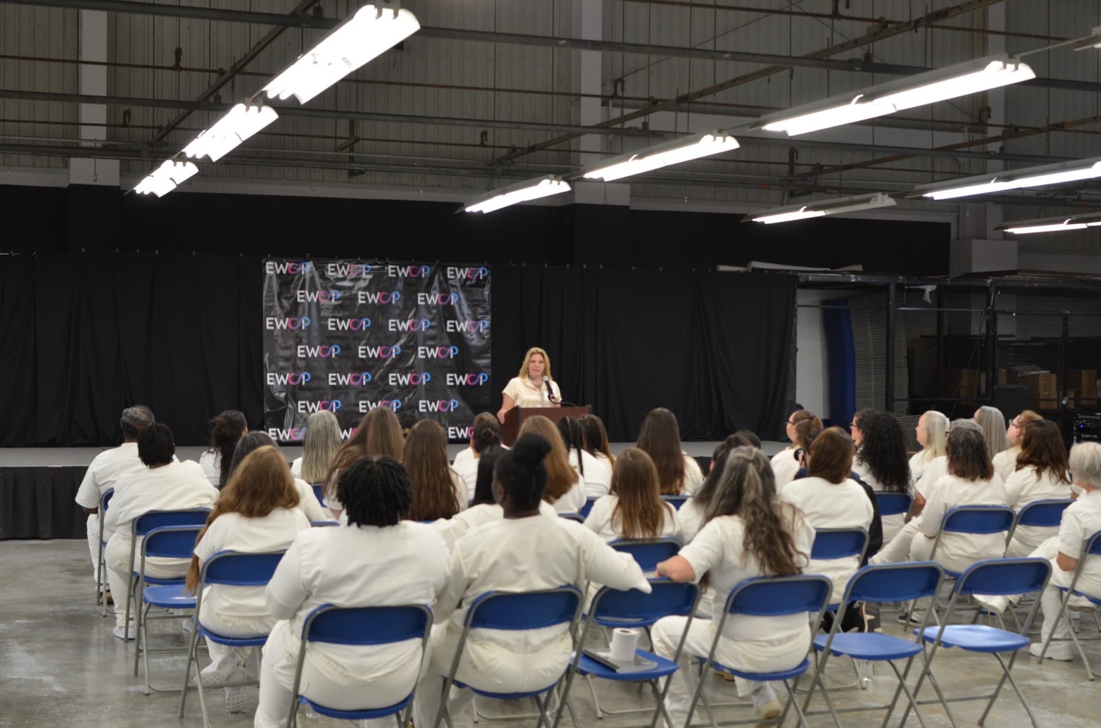 A speaker at a lectern addressing an audience seated in rows beside an EWOP backdrop.